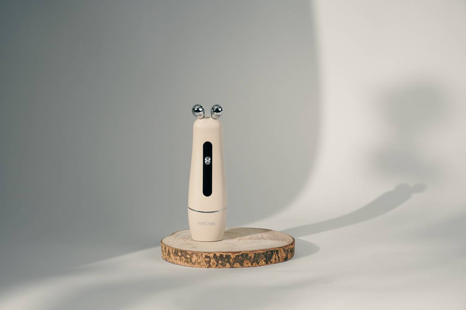 Un rodillo de cuidado de la piel color crema con dos bolas descansa sobre una rodaja de madera.