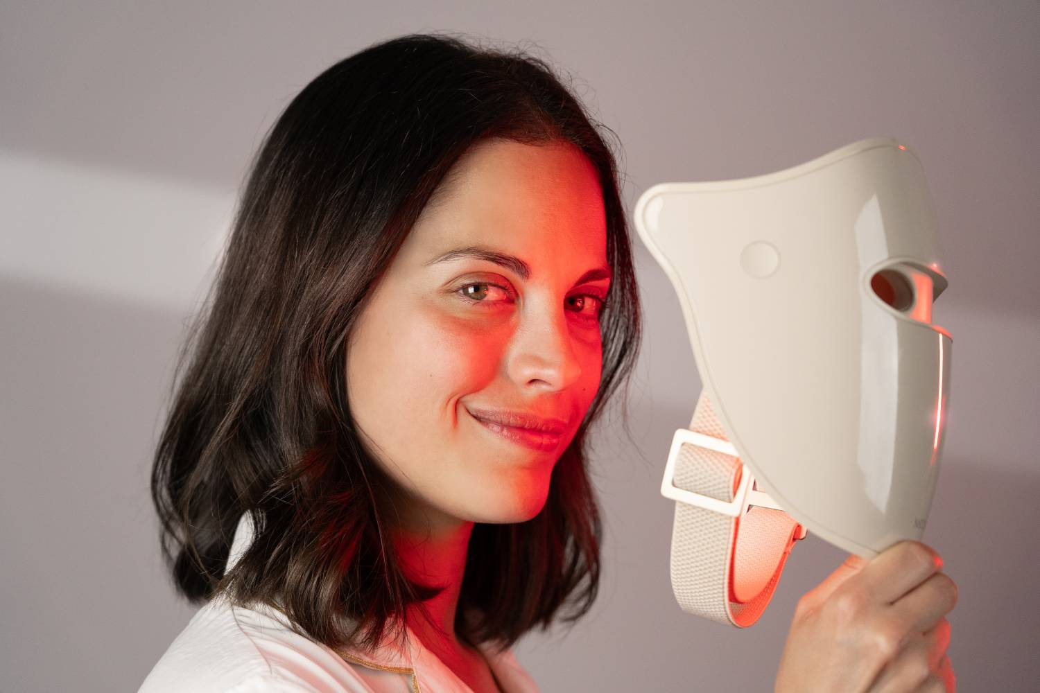 Mujer de pelo oscuro sostiene una mascarilla blanca con luz roja.