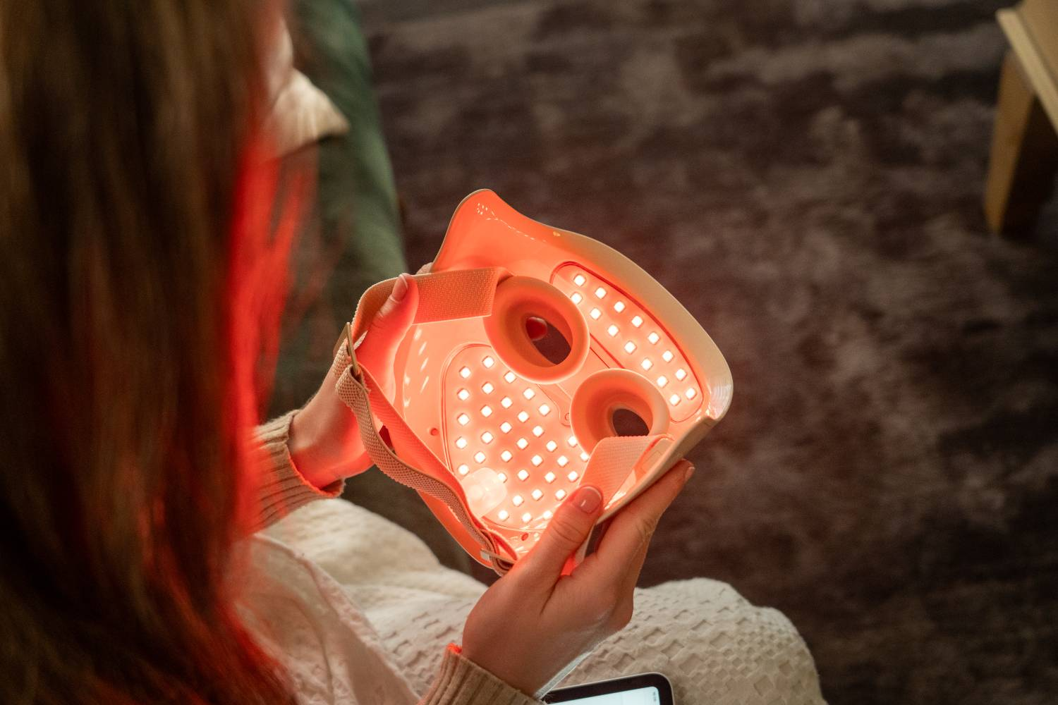 Persona sosteniendo una mascarilla facial LED roja con aberturas para ojos y correas.