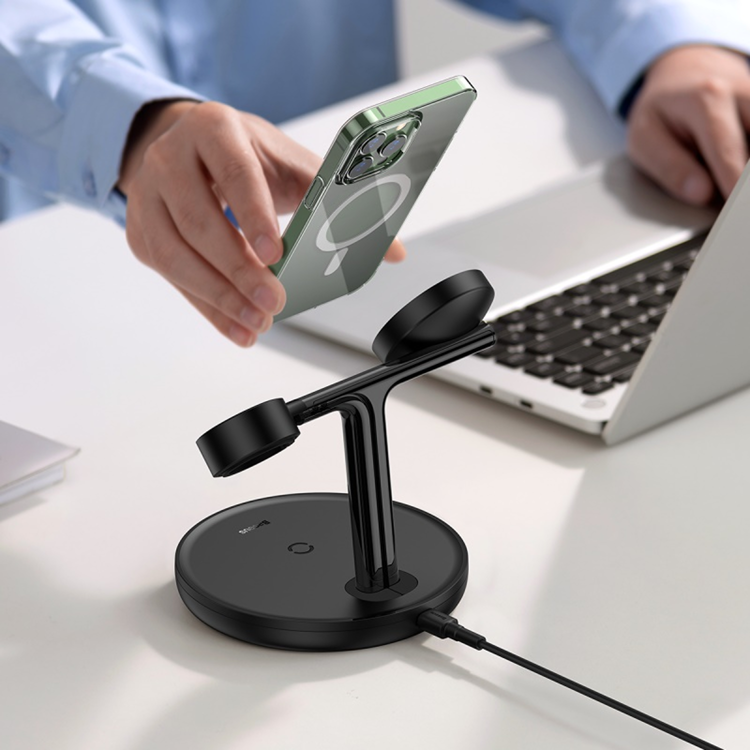 Persona sosteniendo un teléfono verde sobre un cargador negro, portátil detrás.