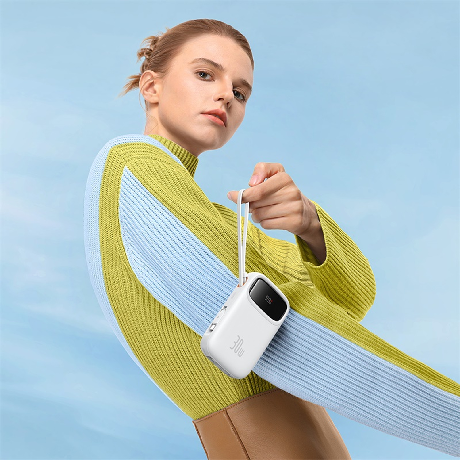Mujer con cargador blanco en la muñeca, suéter a rayas, cielo azul.