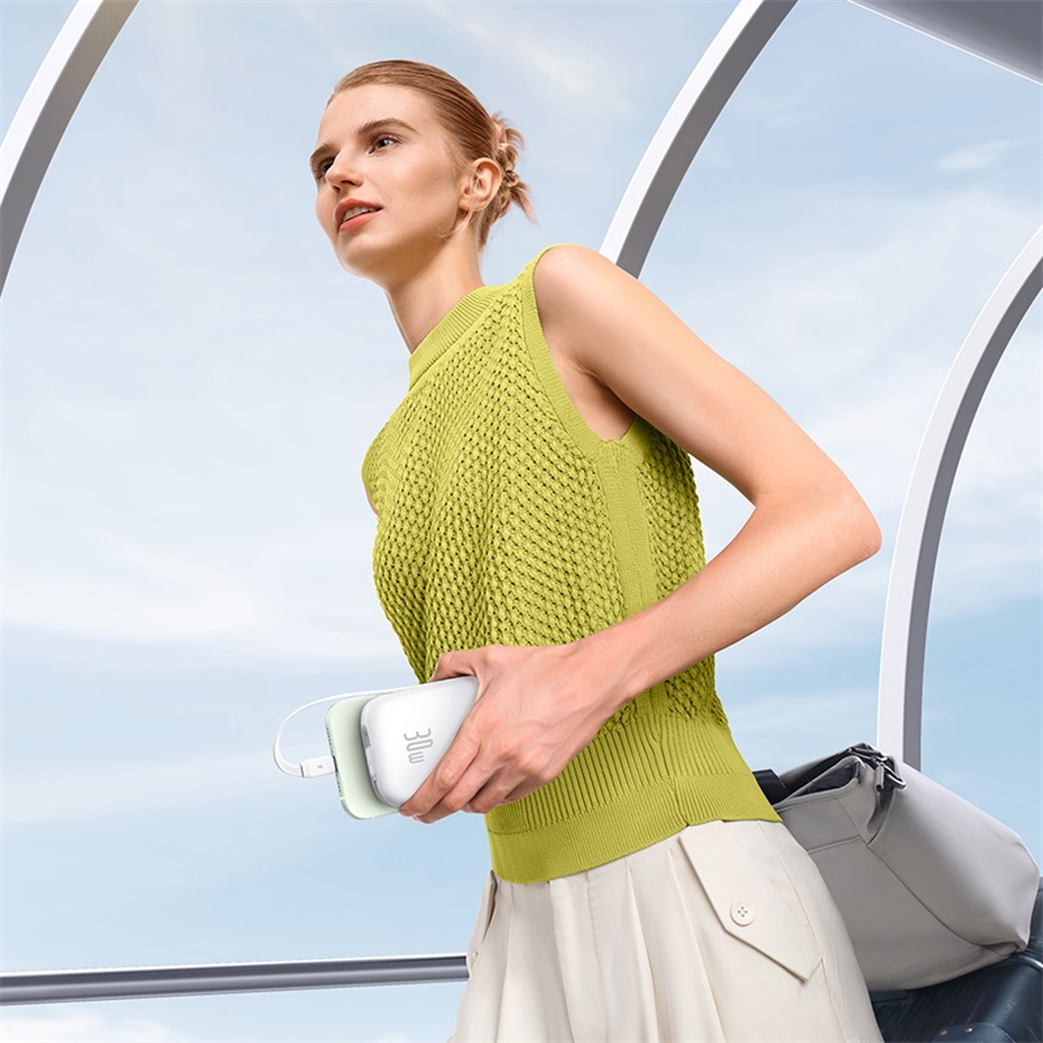 Mujer con batería externa y bolso ante cielo azul.