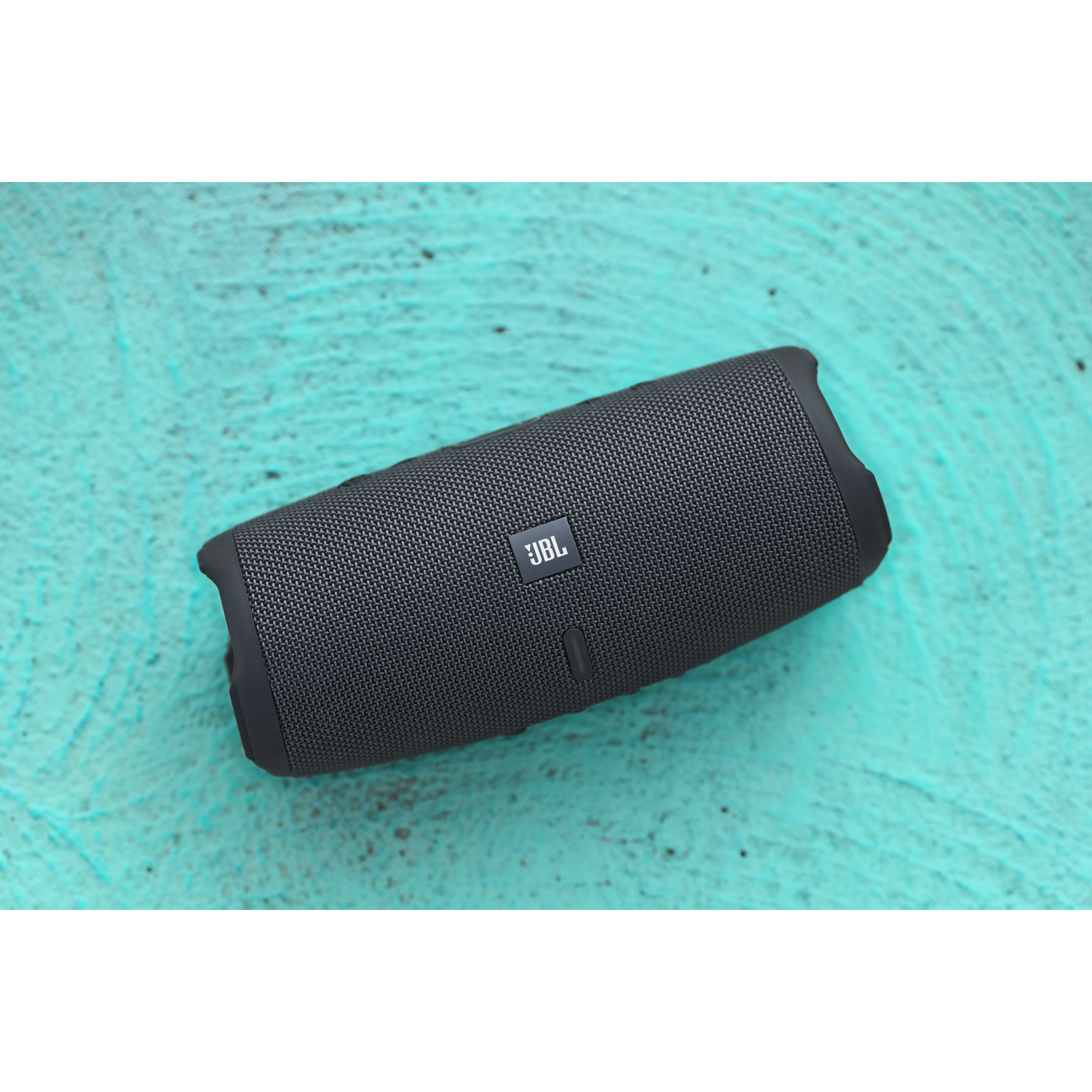 A black JBL speaker rests on a turquoise surface.