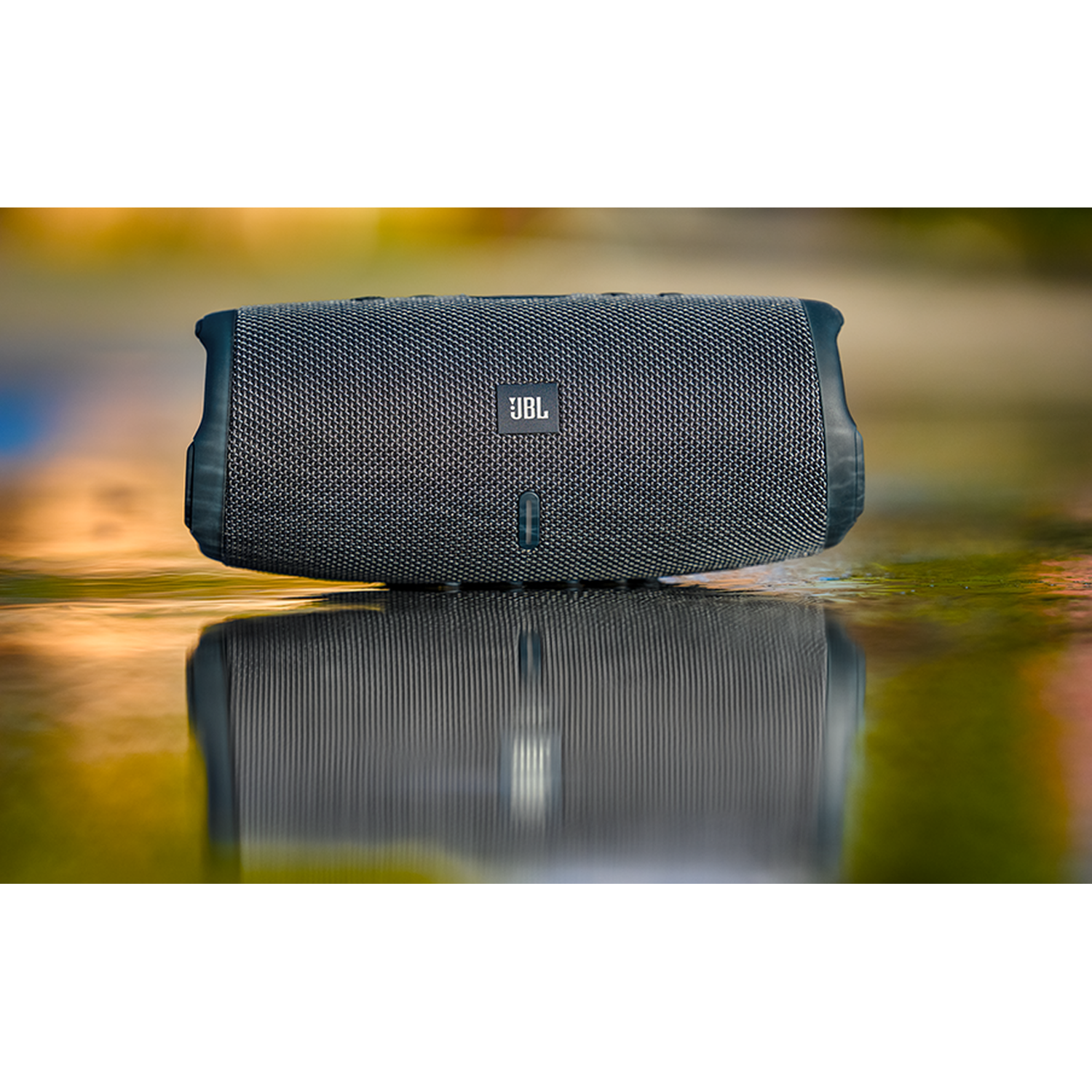 Gray JBL speaker on a wet surface with reflection. Blurred background.