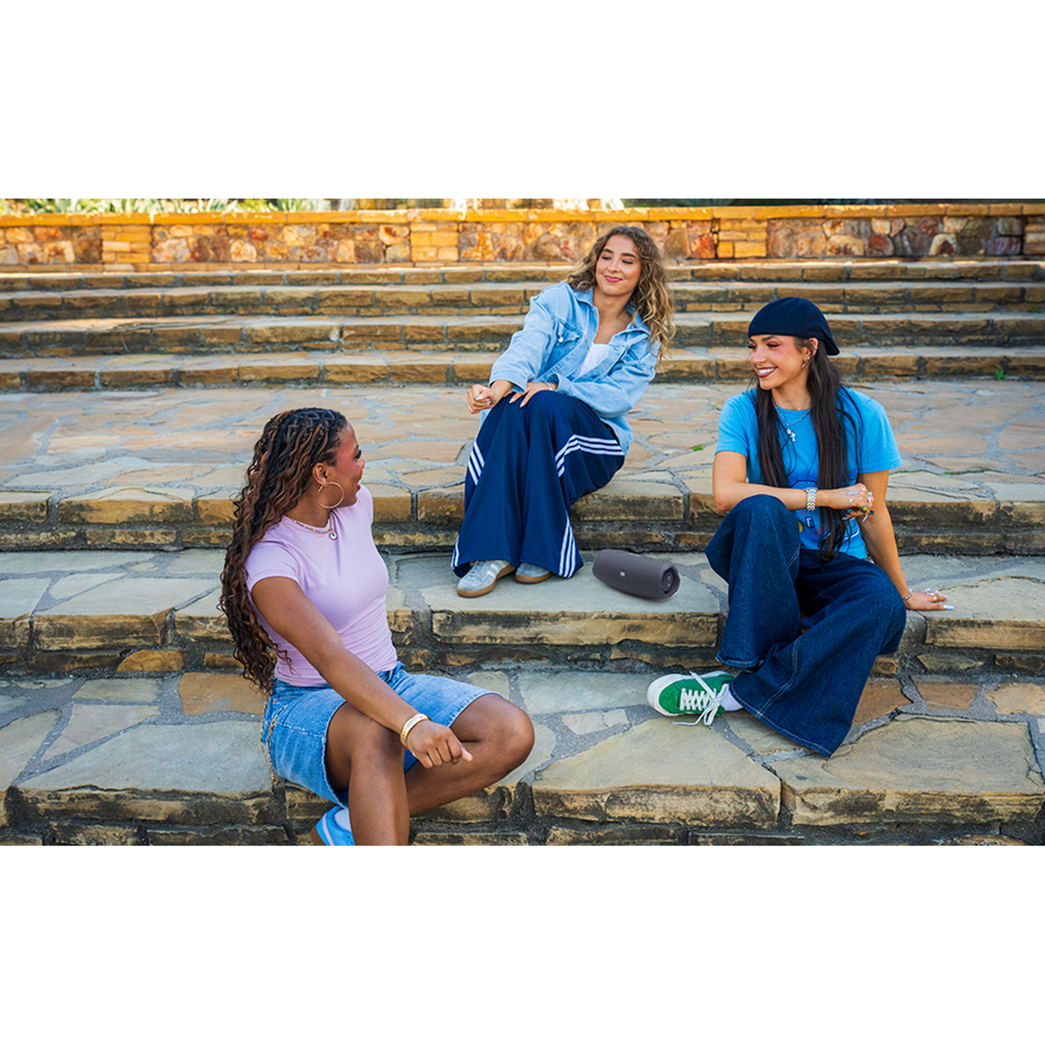 Three young women sit on stone steps with a speaker in front of them.
