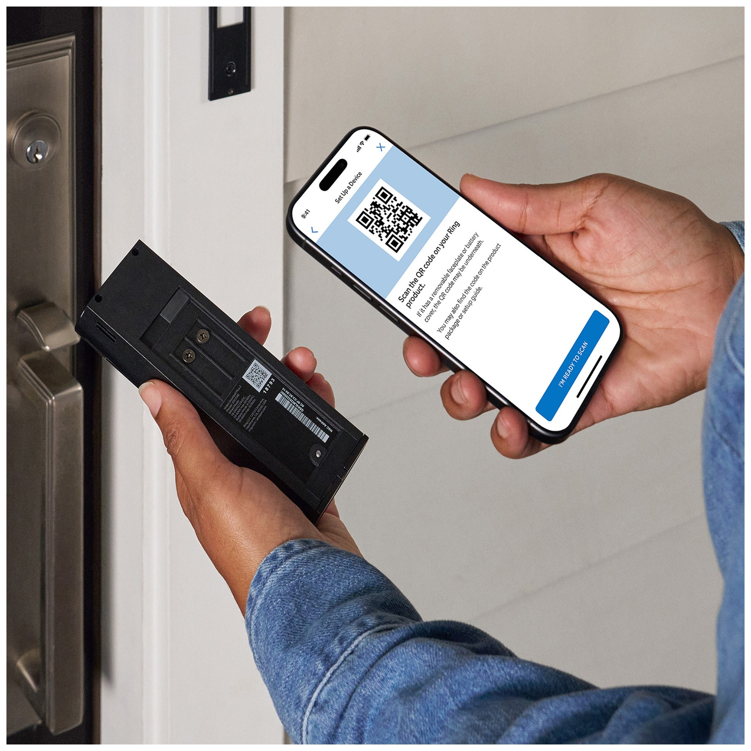A person holds a smartphone with a QR code and a black device in front of a door.