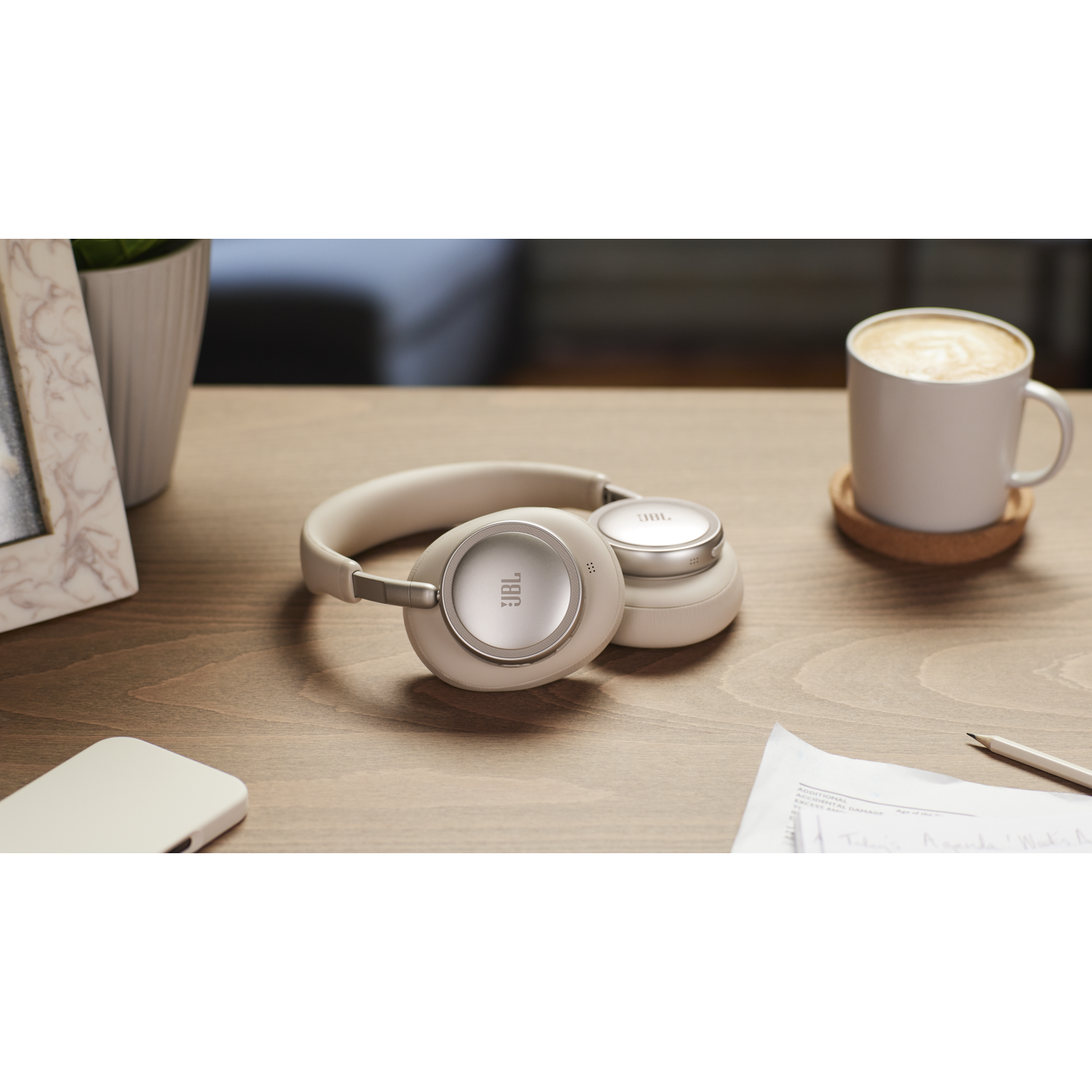 Beige headphones rest on a wooden desk beside a coffee cup.