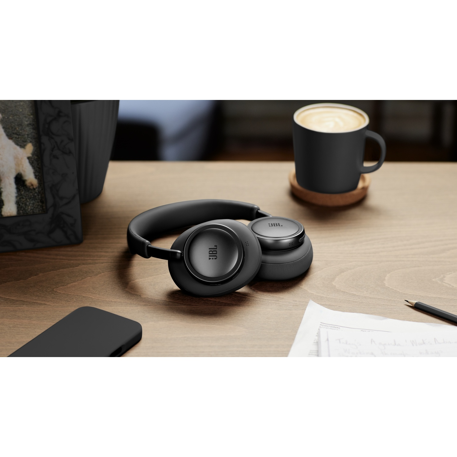 Casque JBL noir, smartphone, tasse à café et notes sur un bureau en bois.