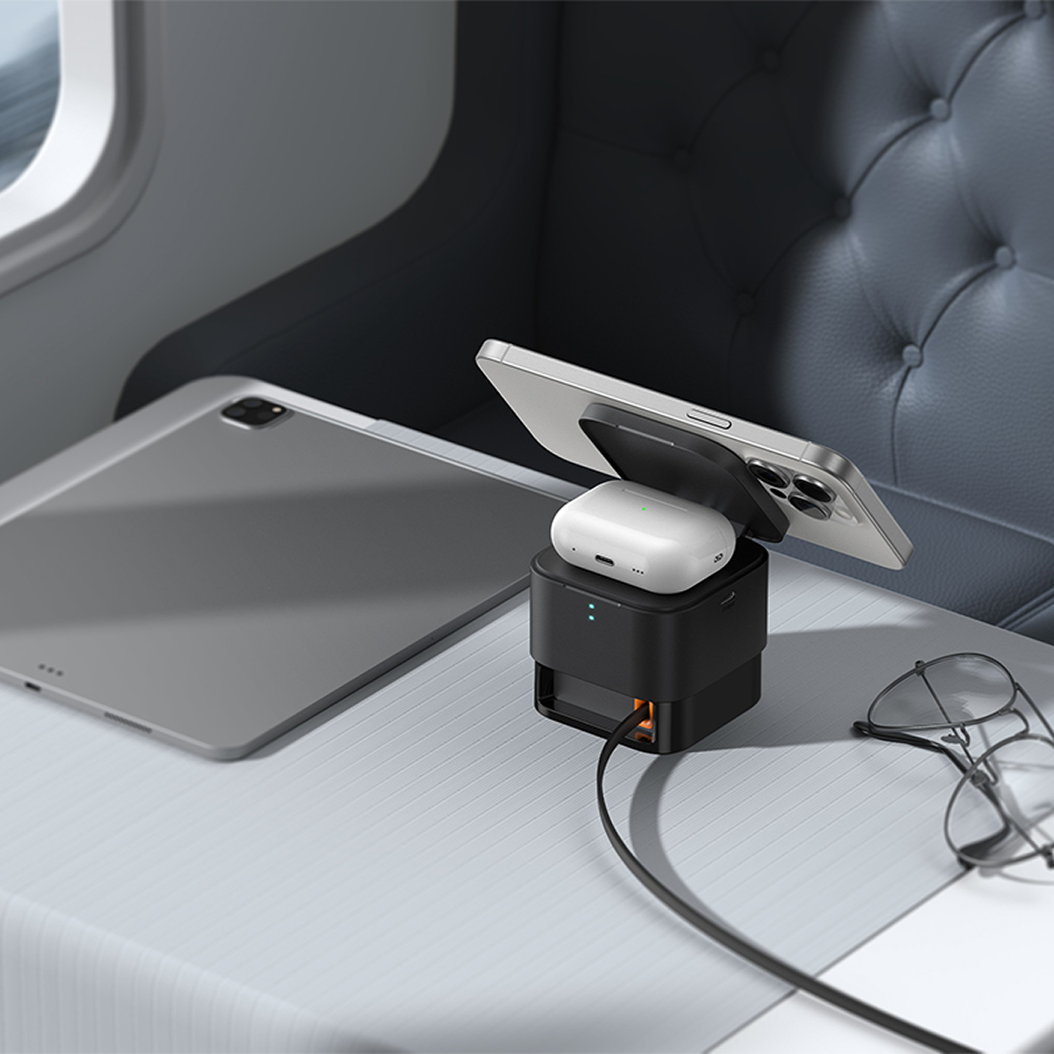 Un soporte de carga negro sostiene un teléfono y auriculares en una mesa con una tableta y gafas.