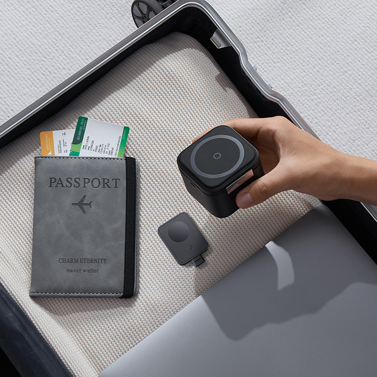 Pasaporte gris con tarjetas de embarque, cargador negro y portátil en maleta.