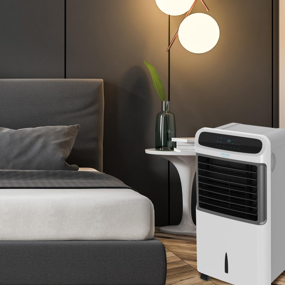 Un enfriador de aire blanco junto a una cama en un dormitorio moderno con mesita de noche.