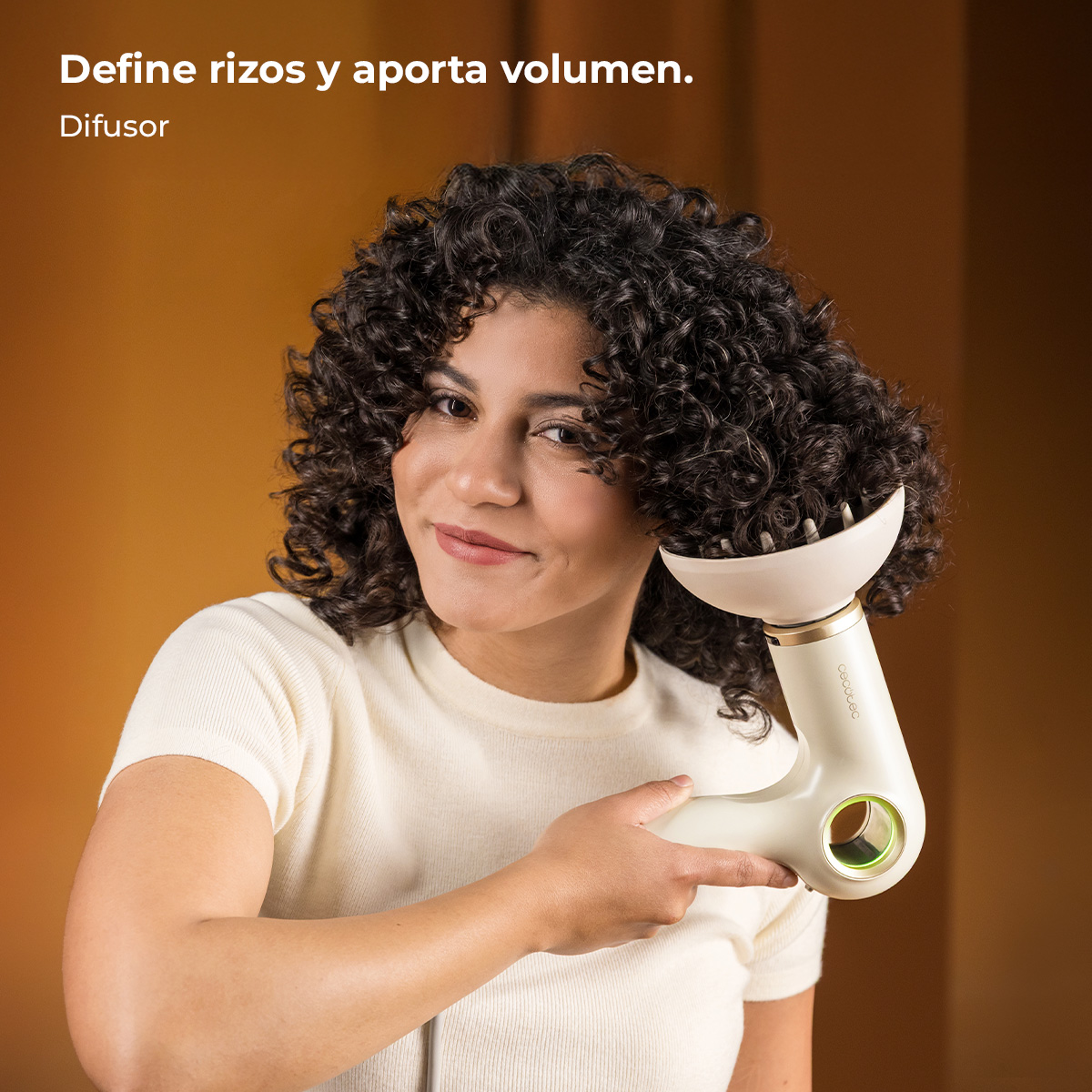 Mujer con pelo rizado usando un difusor crema en su pelo. Fondo naranja.