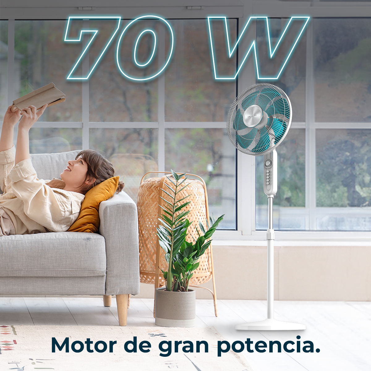 Mujer lee libro en sofá cerca de ventilador blanco con aspas turquesas. Texto: 70 W.