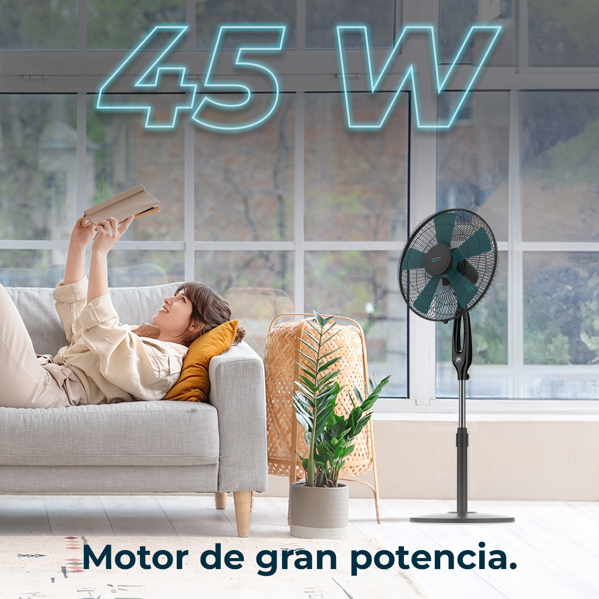 Una mujer yace en un sofá leyendo un libro. Un ventilador está cerca.