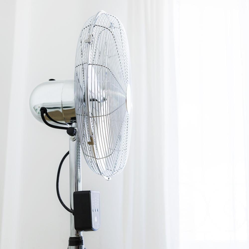 Un ventilador de pie plateado con rejilla redonda y panel de control negro.