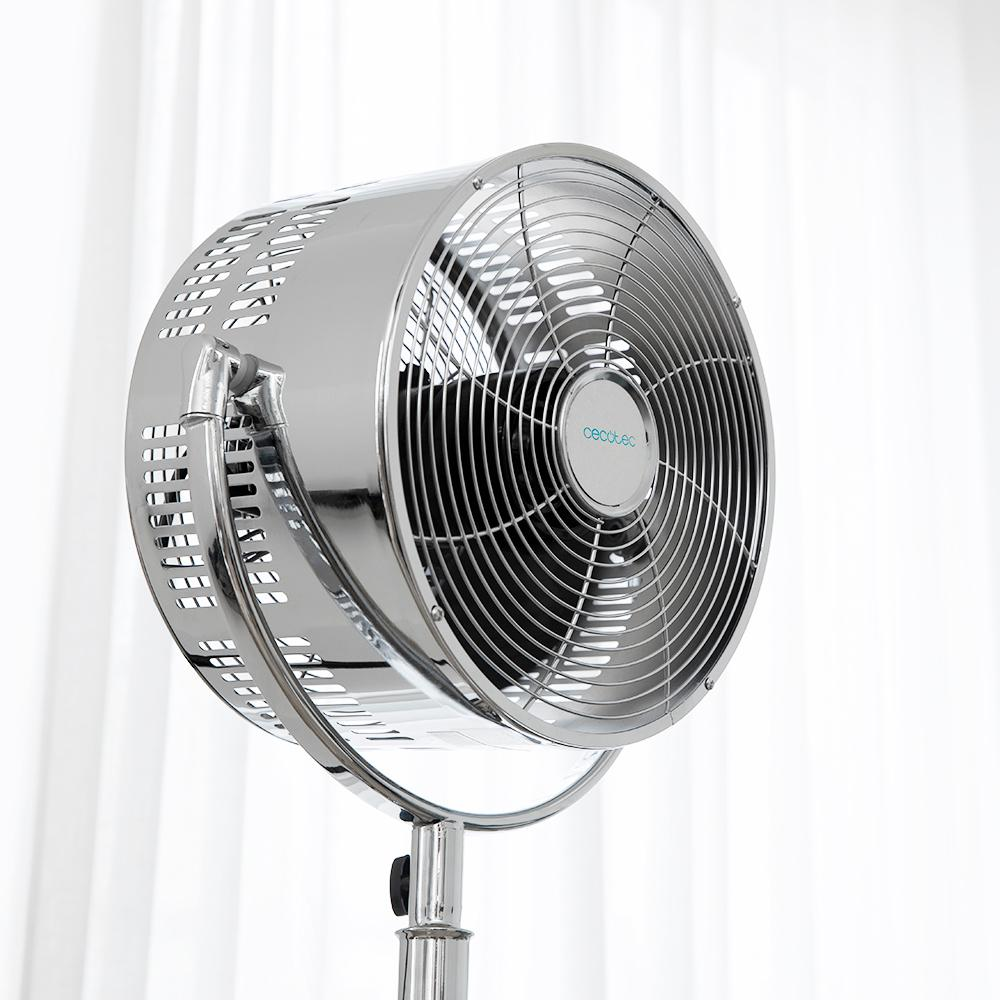 Se muestra un ventilador de pie cromado con rejilla circular y logo frente a una cortina blanca.