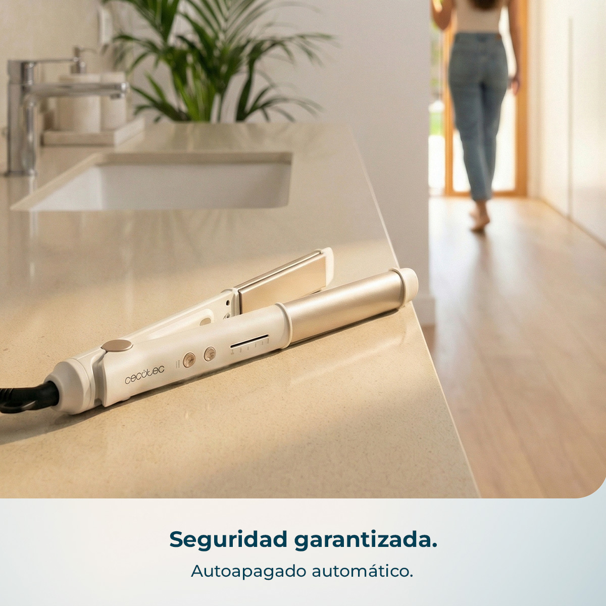 Una plancha de pelo blanca y dorada descansa sobre una encimera beige. Una persona se aleja al fondo.
