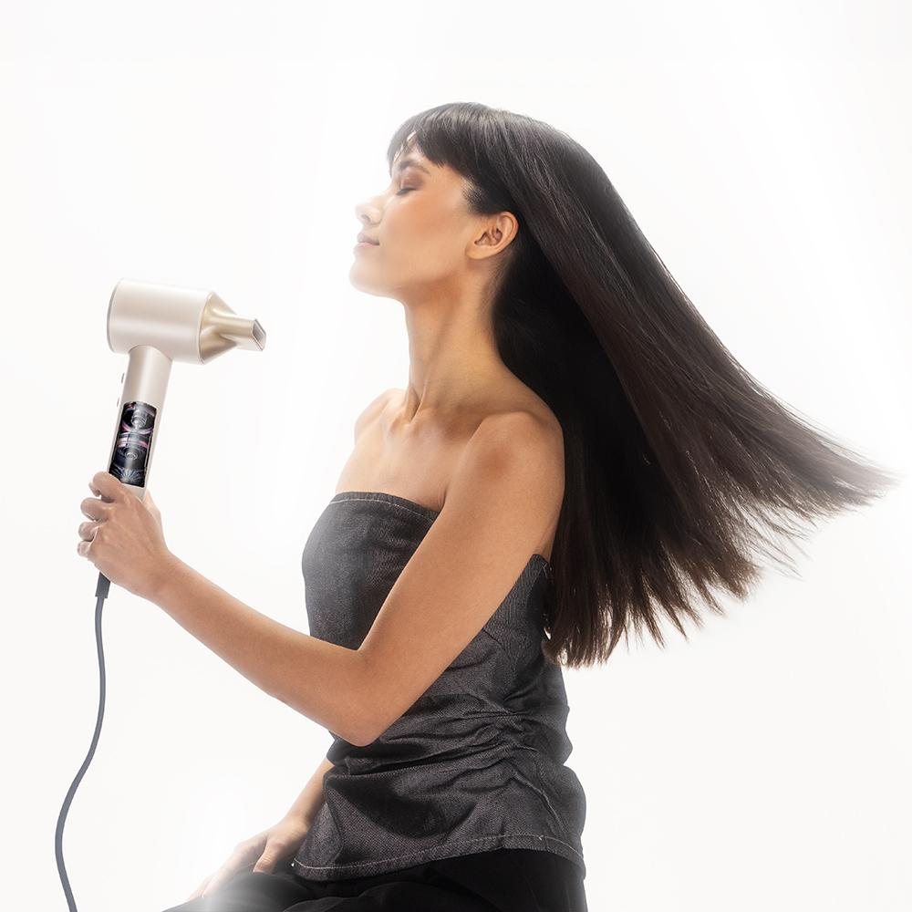 Mujer con pelo largo y oscuro secándose el pelo con un secador plateado.