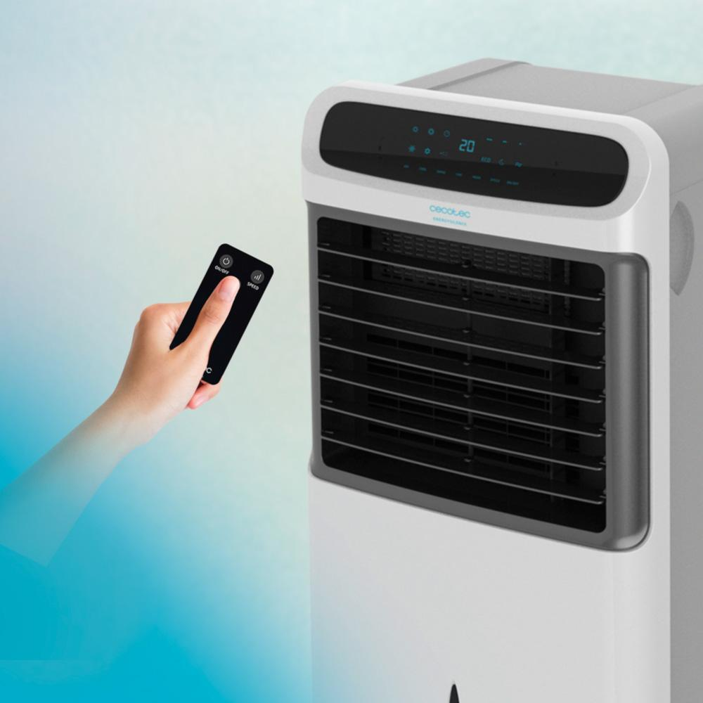 Una mano sostiene un mando a distancia negro, apuntándolo hacia un enfriador de aire blanco y gris con pantalla digital.