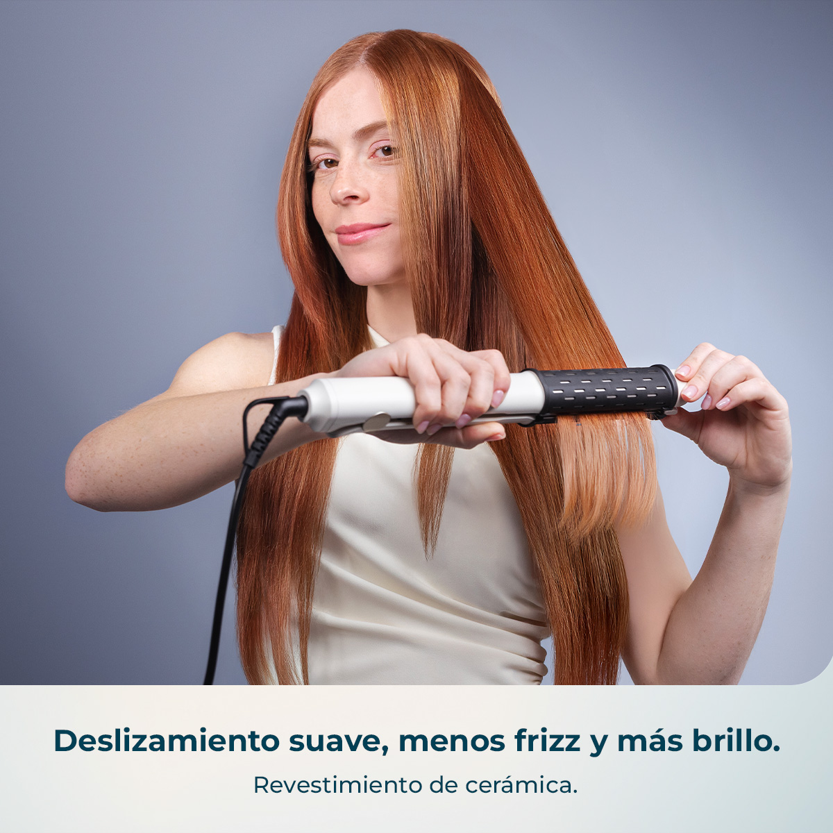 Mujer de pelo rojo largo se alisa el pelo con una plancha blanca.