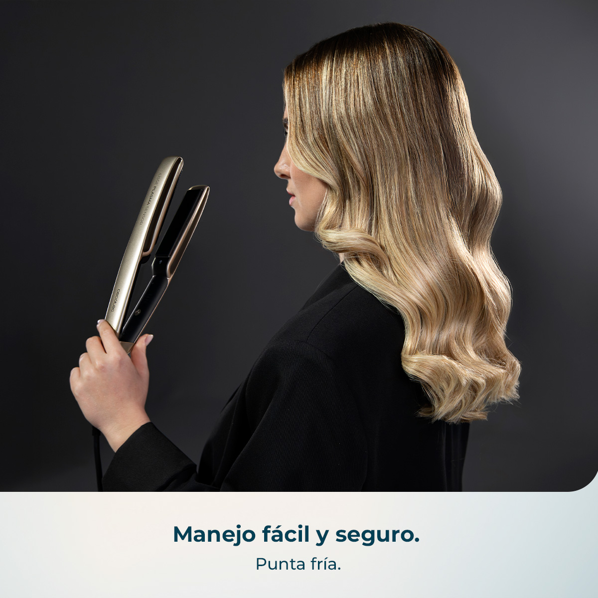 Una mujer con cabello rubio sostiene una plancha plateada sobre fondo oscuro.