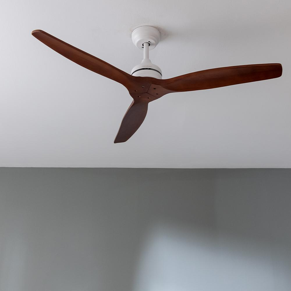 Un ventilador de techo con tres aspas de madera marrones sobre un techo blanco.