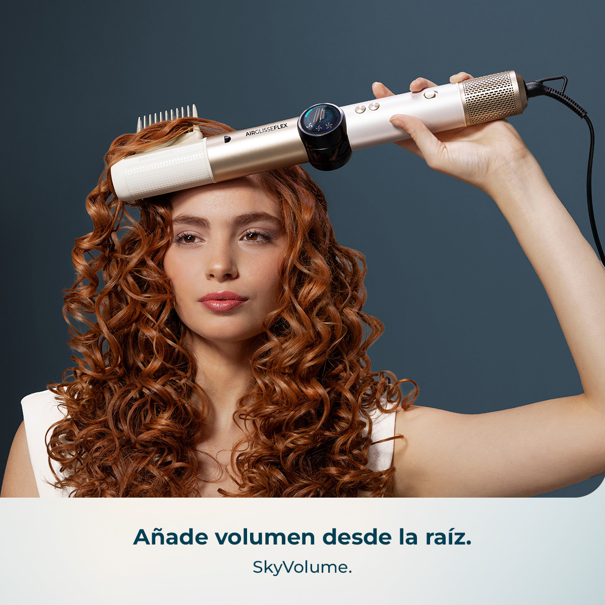 Mujer con cabello rizado usa herramienta dorada para volumen en raíces.