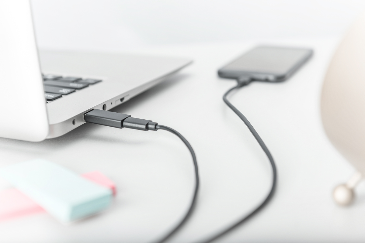 Ein Ladekabel verbindet einen Laptop mit einem Smartphone auf einem weißen Schreibtisch.