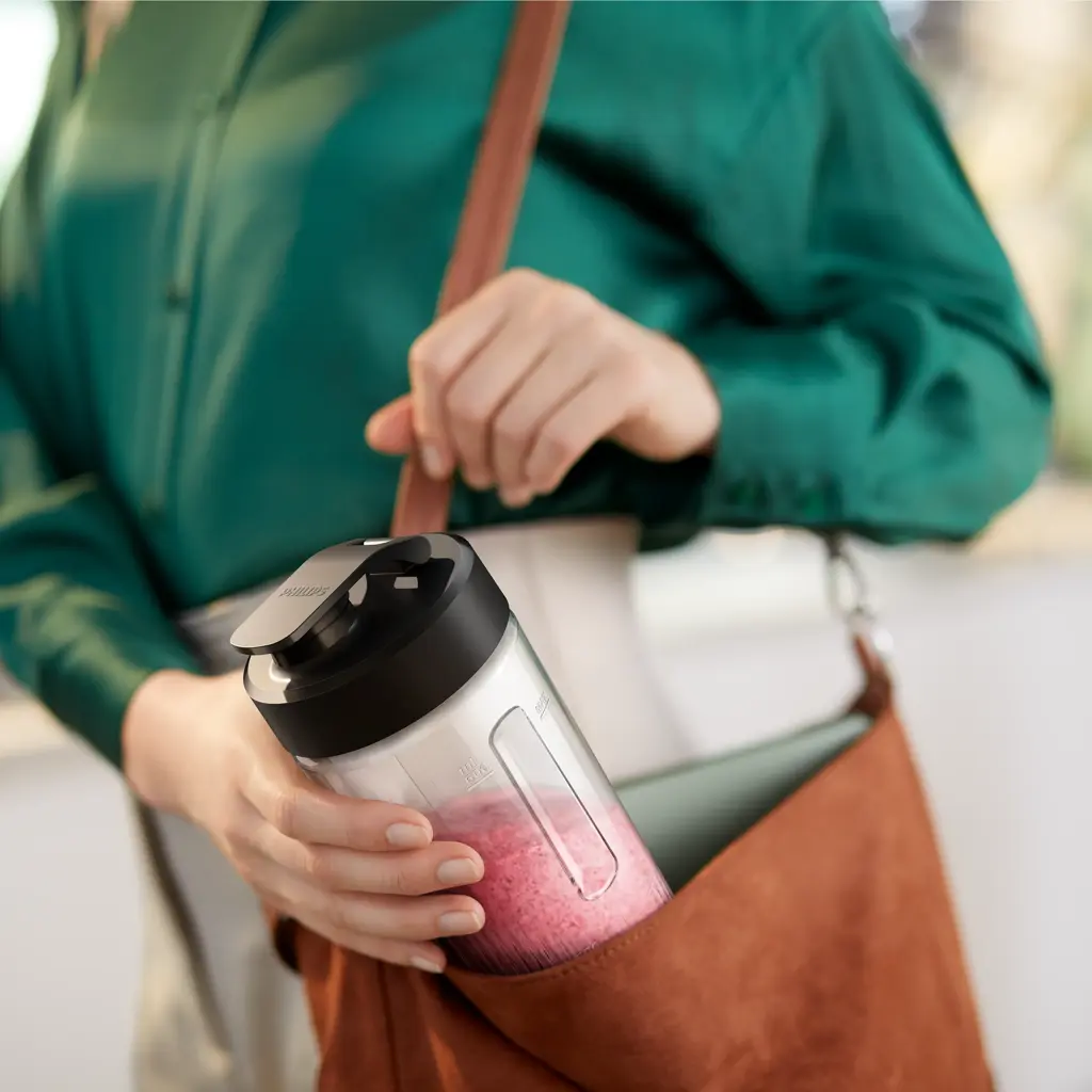 Personne en chemise verte met une bouteille de smoothie rose dans un sac marron.