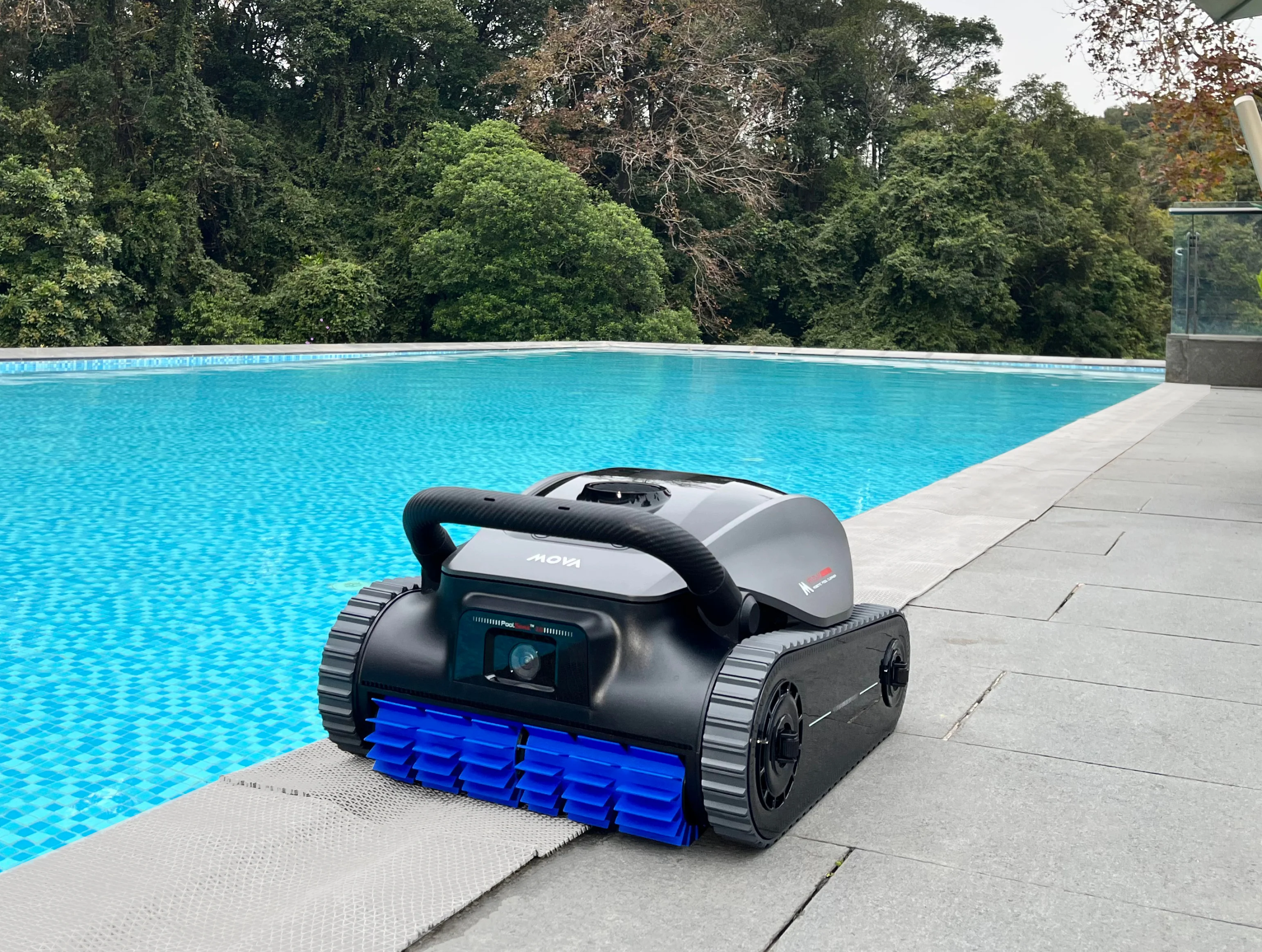 Ein Poolroboter mit blauen Bürsten steht am Rand eines blauen Pools vor üppigem Grün.
