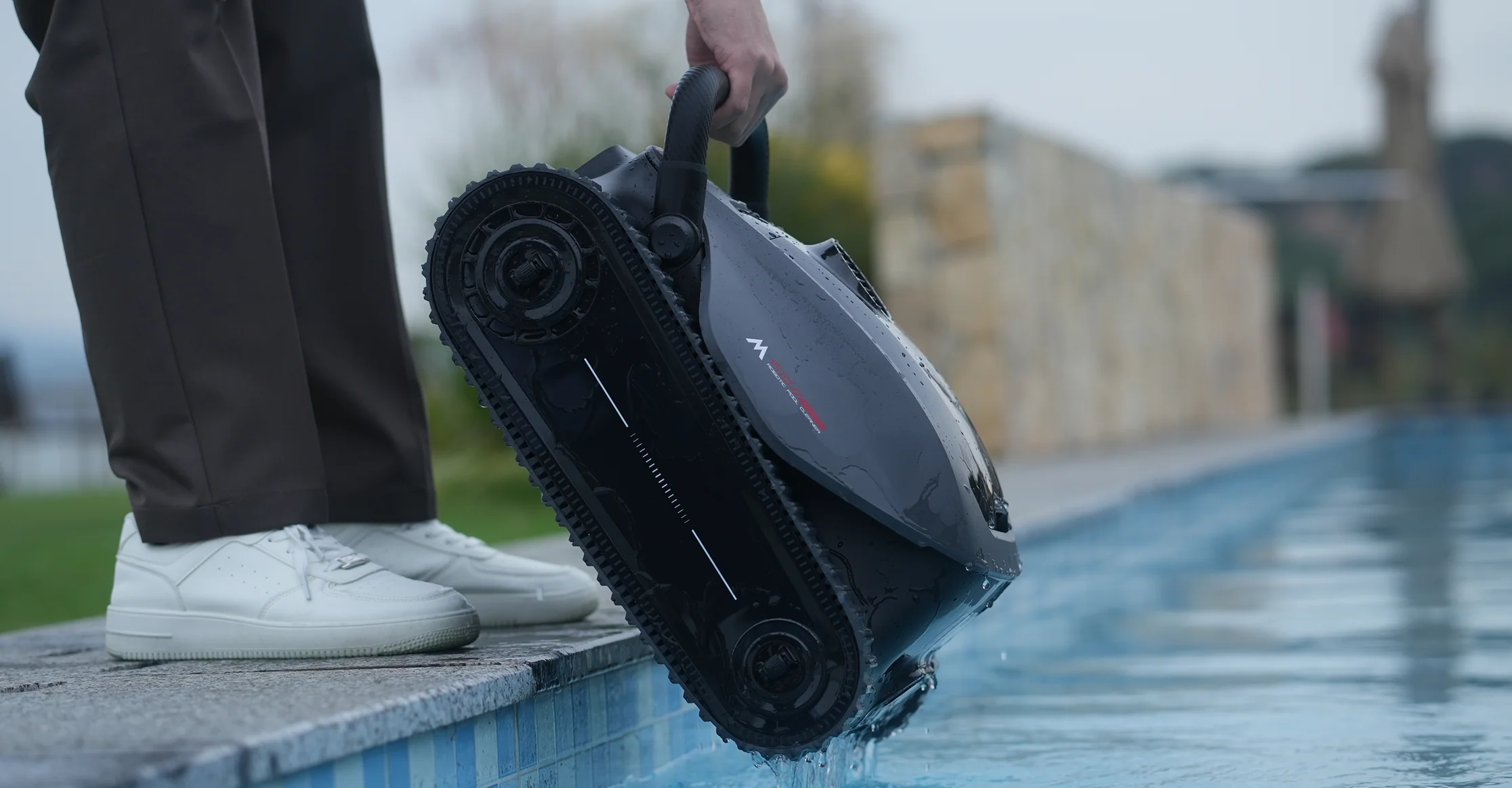 Ein Mann hält einen schwarzen Poolroboter am Griff über dem Wasser.