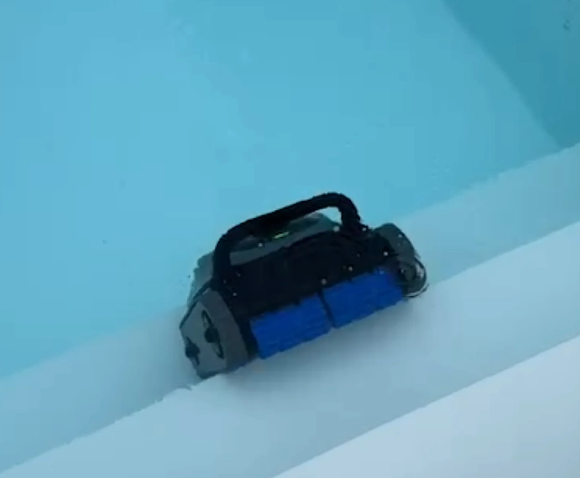 Ein blauer und grauer Poolroboter fährt über weiße Stufen in klarem Wasser.