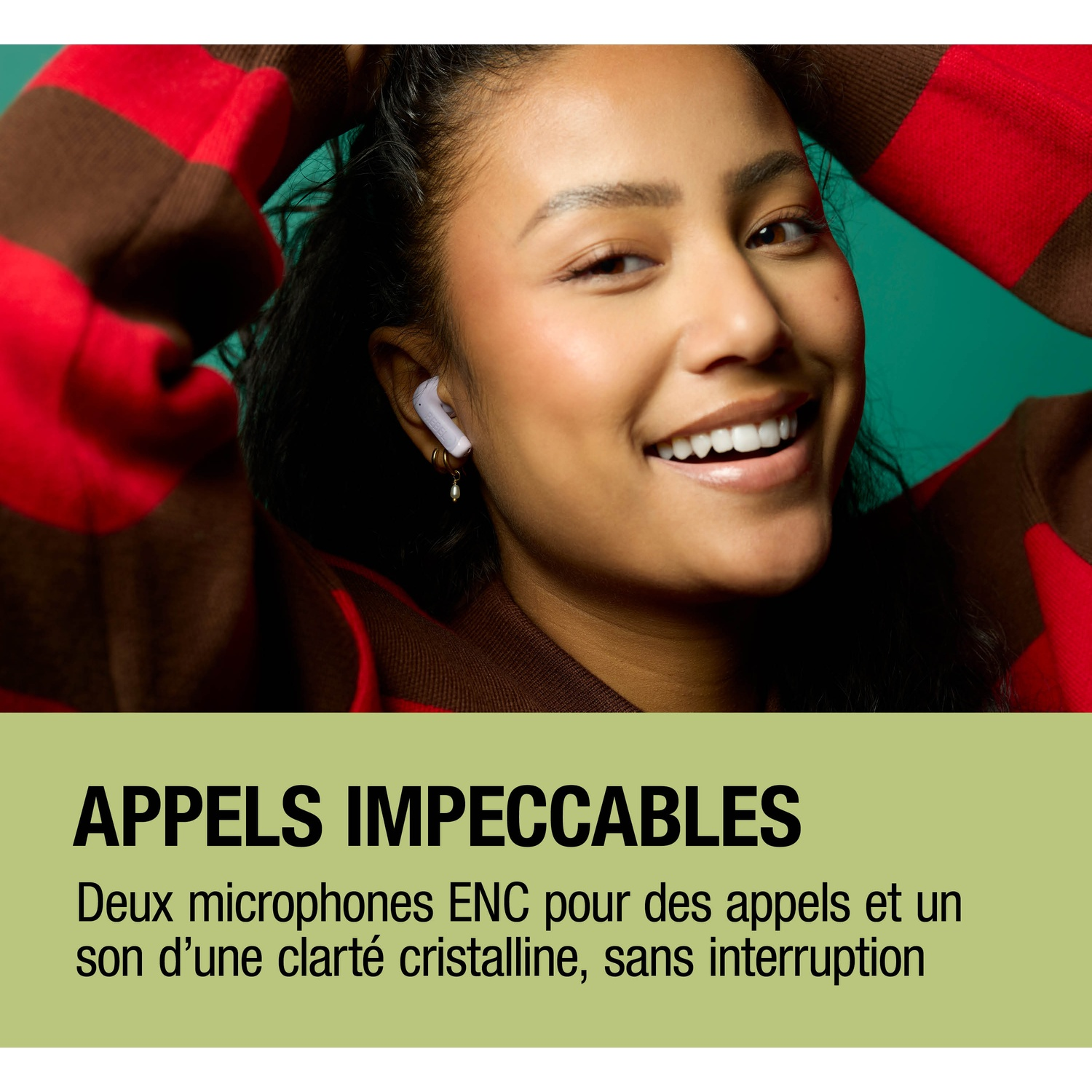 Une femme avec un écouteur sourit, portant un pull à rayures rouges et marron.