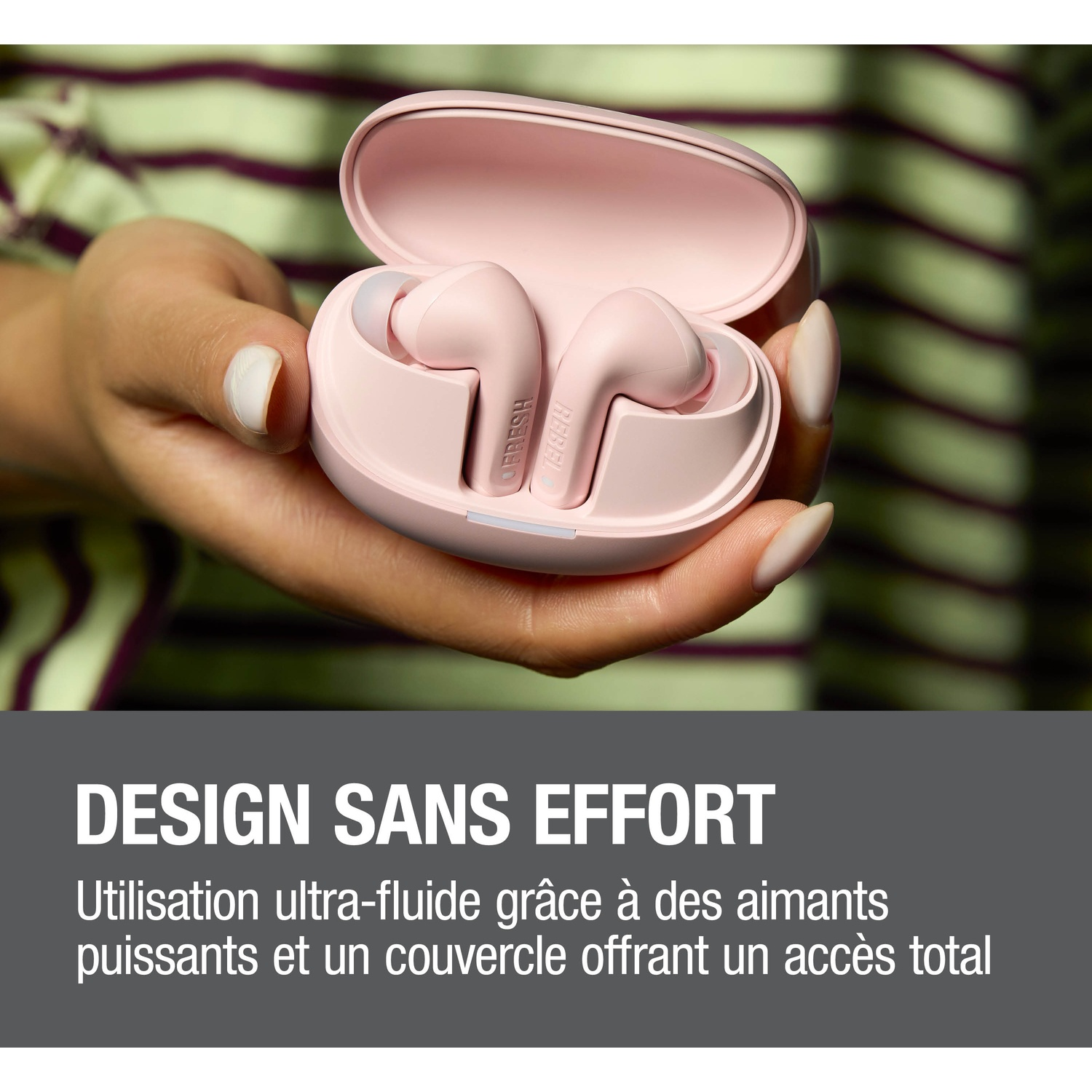 Une main tient un étui de chargement rose avec des écouteurs. Fond rayé.