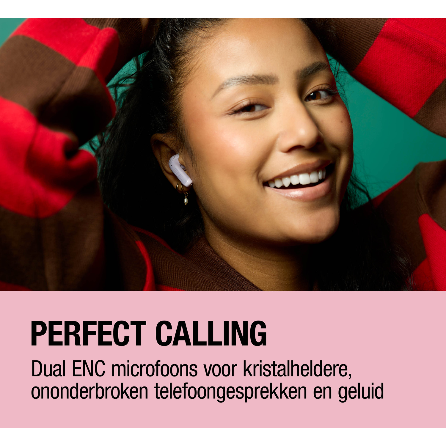 A woman with an earbud smiles. She wears a red and brown sweater.