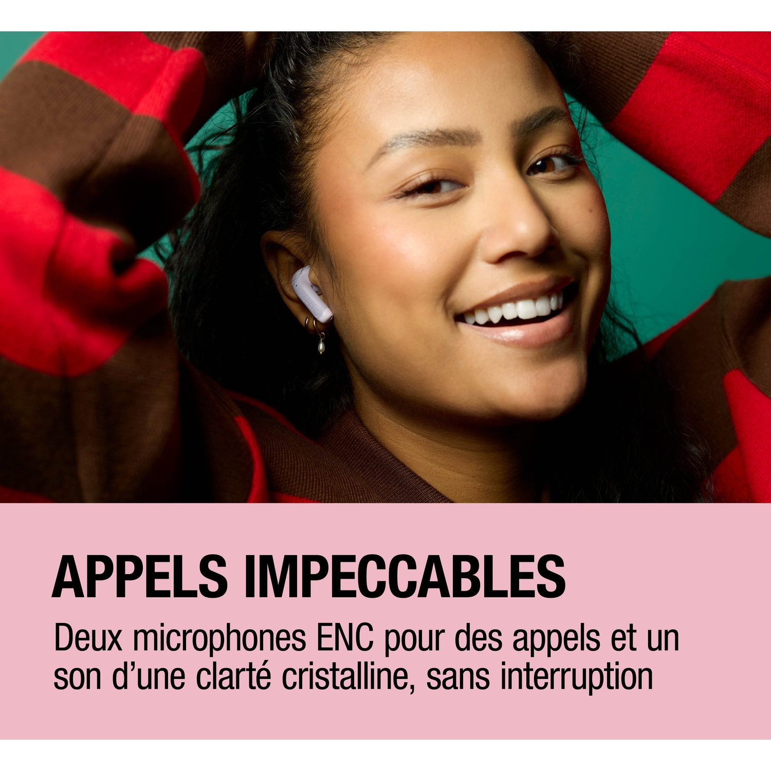 Une femme avec des écouteurs blancs sourit. Elle porte un pull rouge et marron.