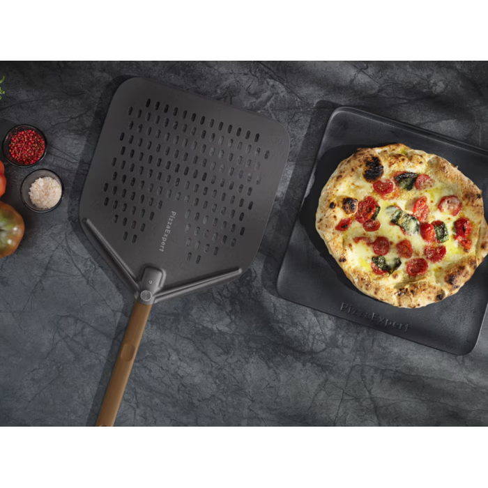 Egy kerek pizzalapát fa nyéllel egy margherita pizza mellett egy fekete tálcán.