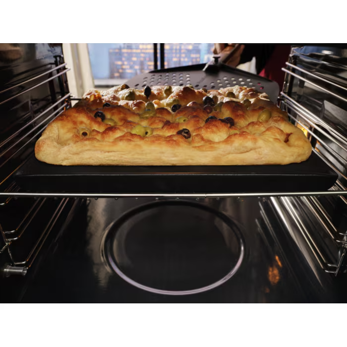 Olívás focacciát vesznek ki a sütőből egy pizzalapáton.