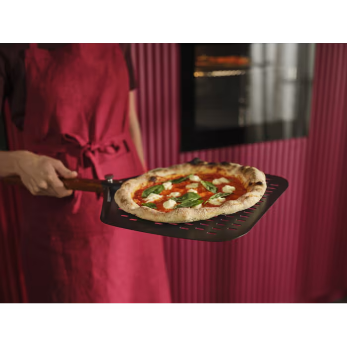 Egy piros kötényes személy egy Margherita pizzát tart egy pizzasütő lapáton.