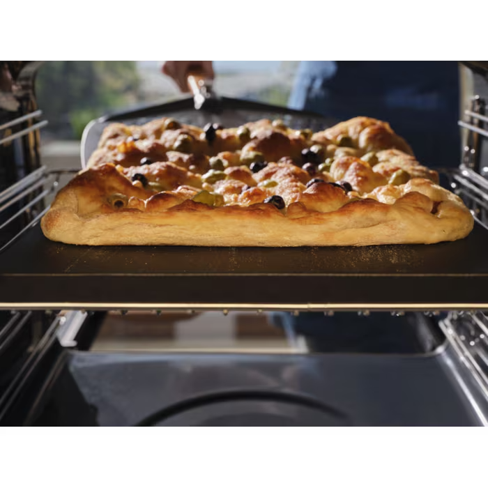 Egy aranybarnára sült, olívás focacciát pizzalapáttal vesznek ki a sütőből.