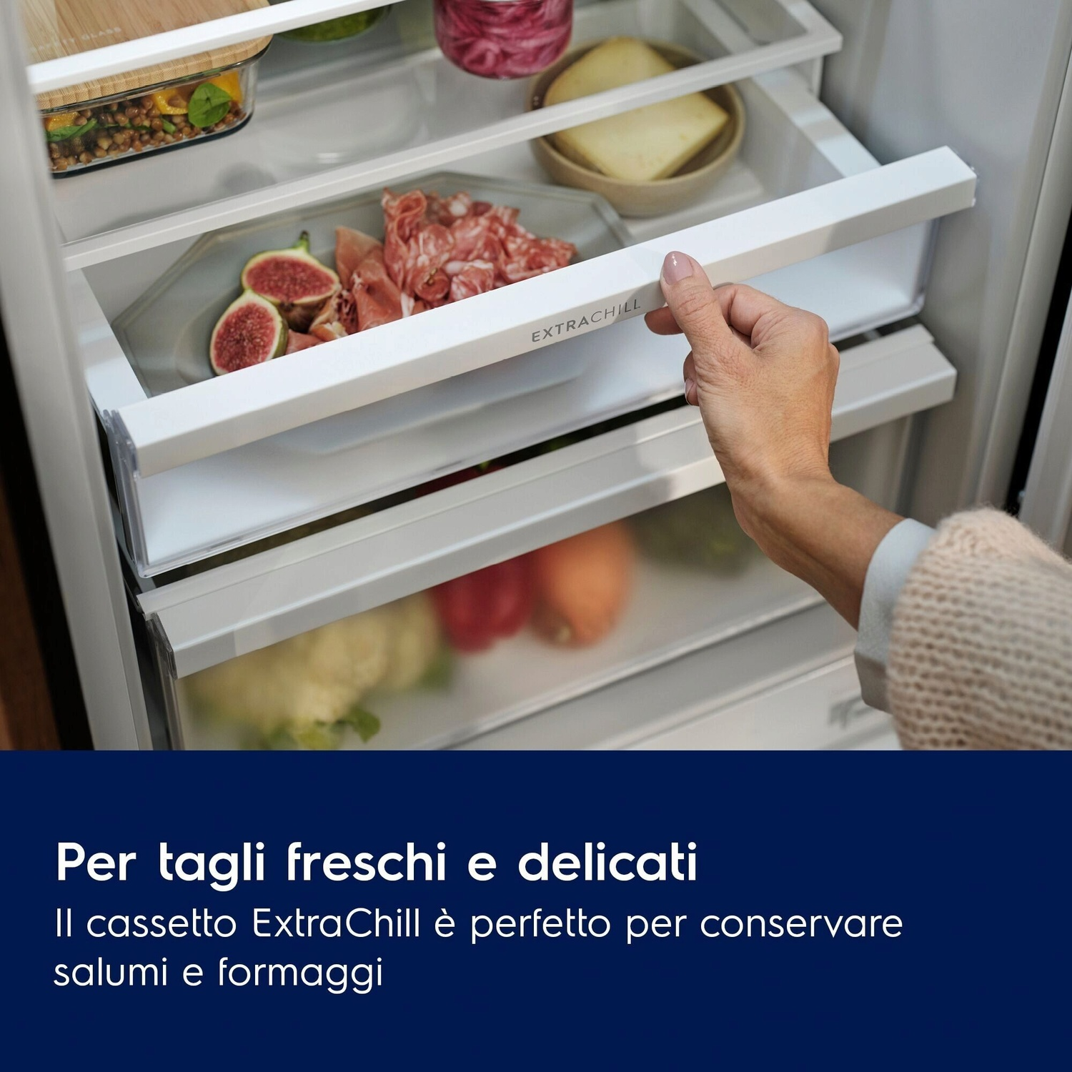 Una mano apre un cassetto del frigo con fichi, salumi e formaggio.
