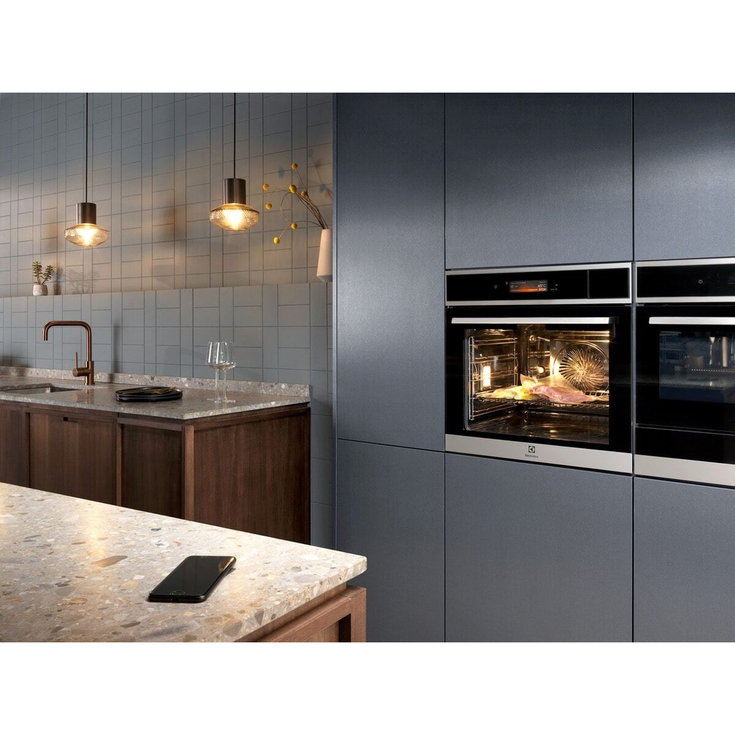 Cucina moderna con forno illuminato che cuoce cibo e un bancone con telefono.