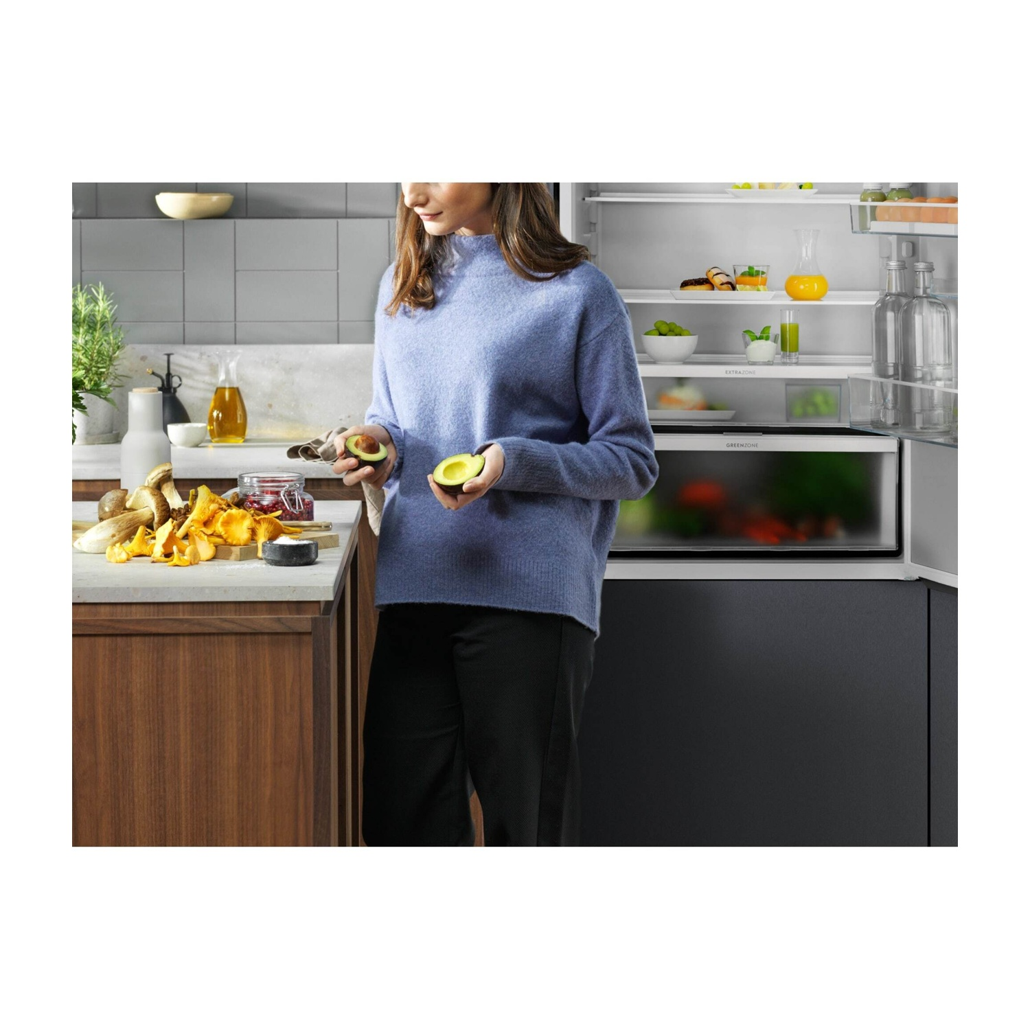 Una donna tiene un avocado in una cucina moderna accanto a un frigorifero aperto.