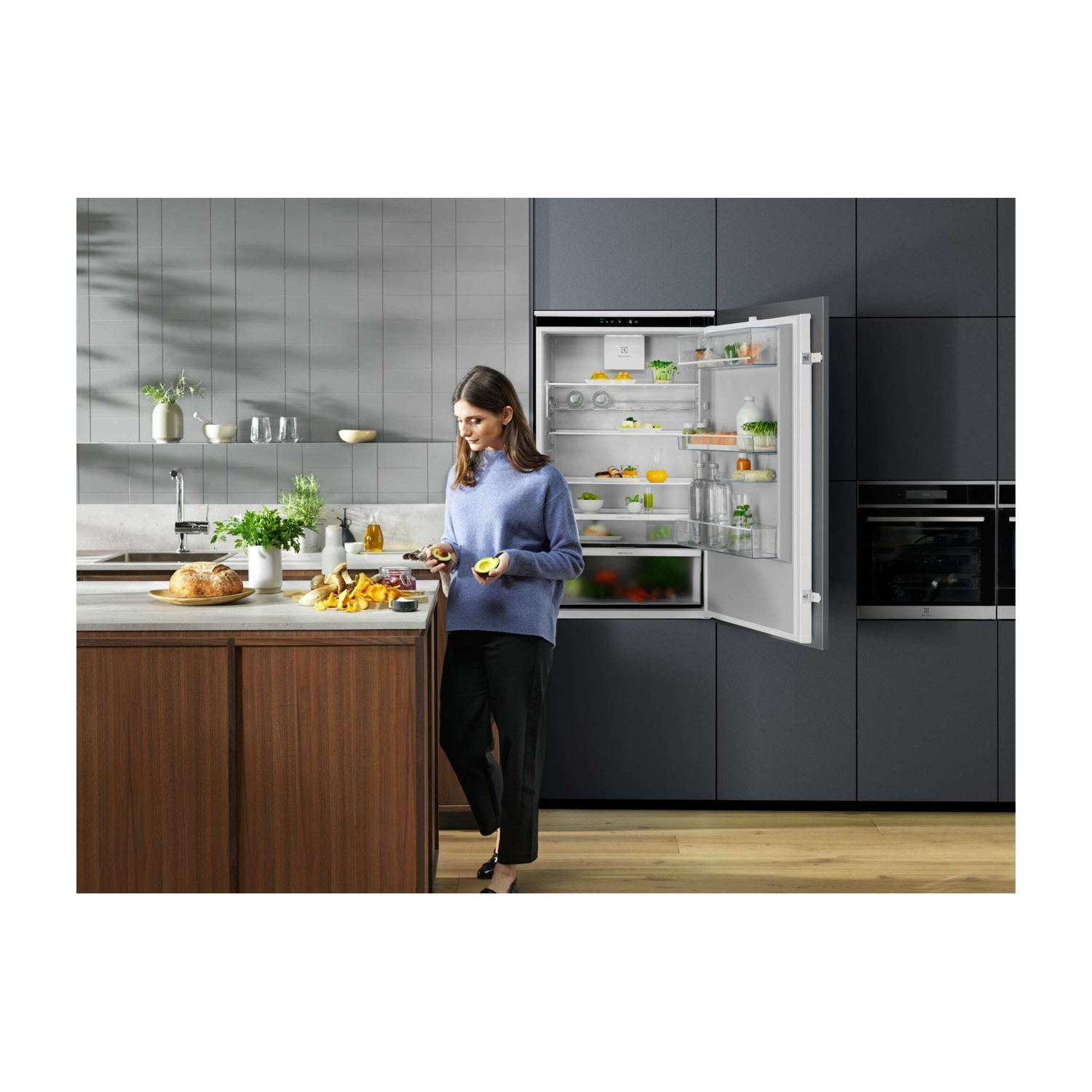 Una donna con un maglione blu è in una cucina moderna, tiene un avocado.