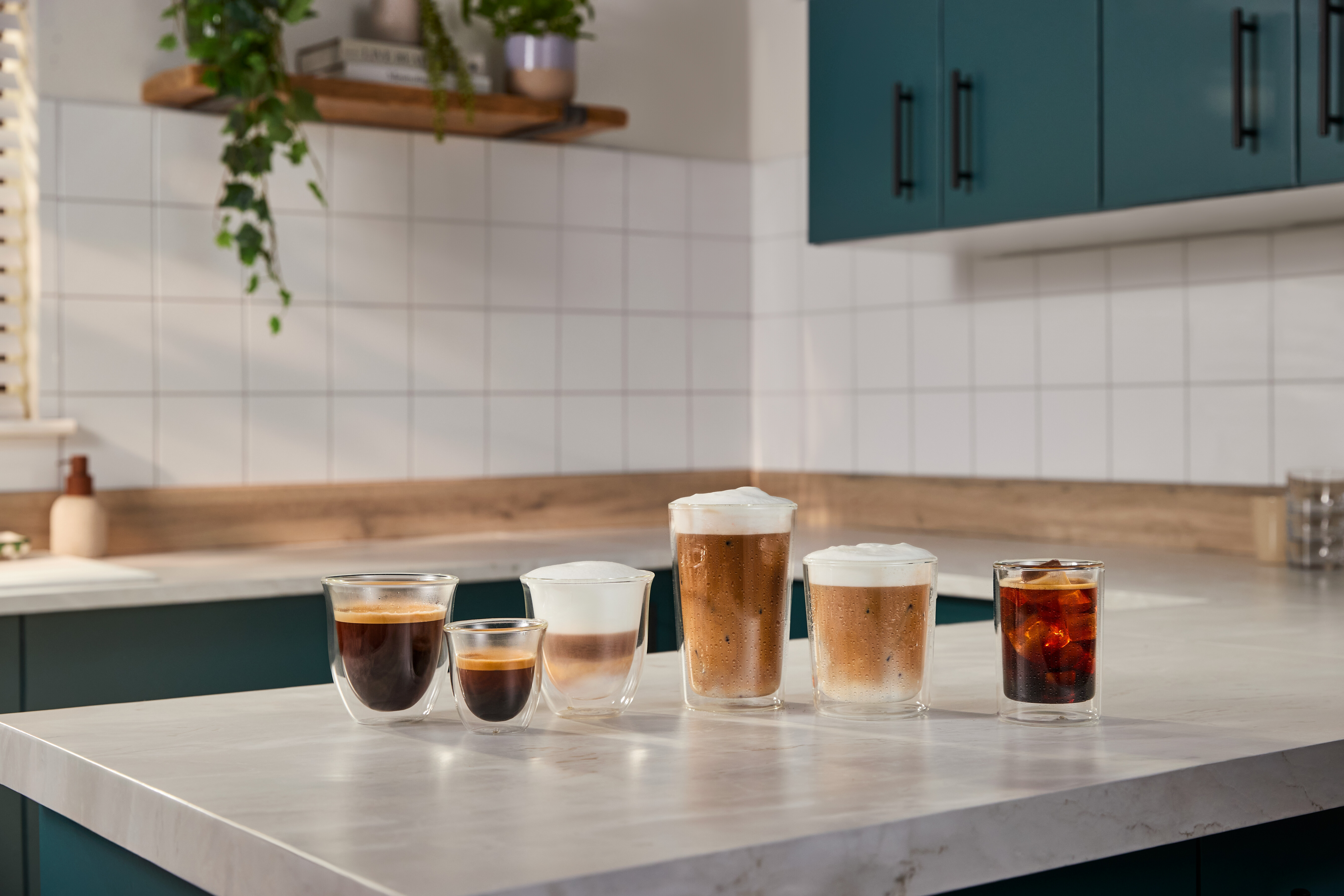 Fünf Gläser mit Kaffeegetränken stehen auf einer Arbeitsplatte in einer Küche.