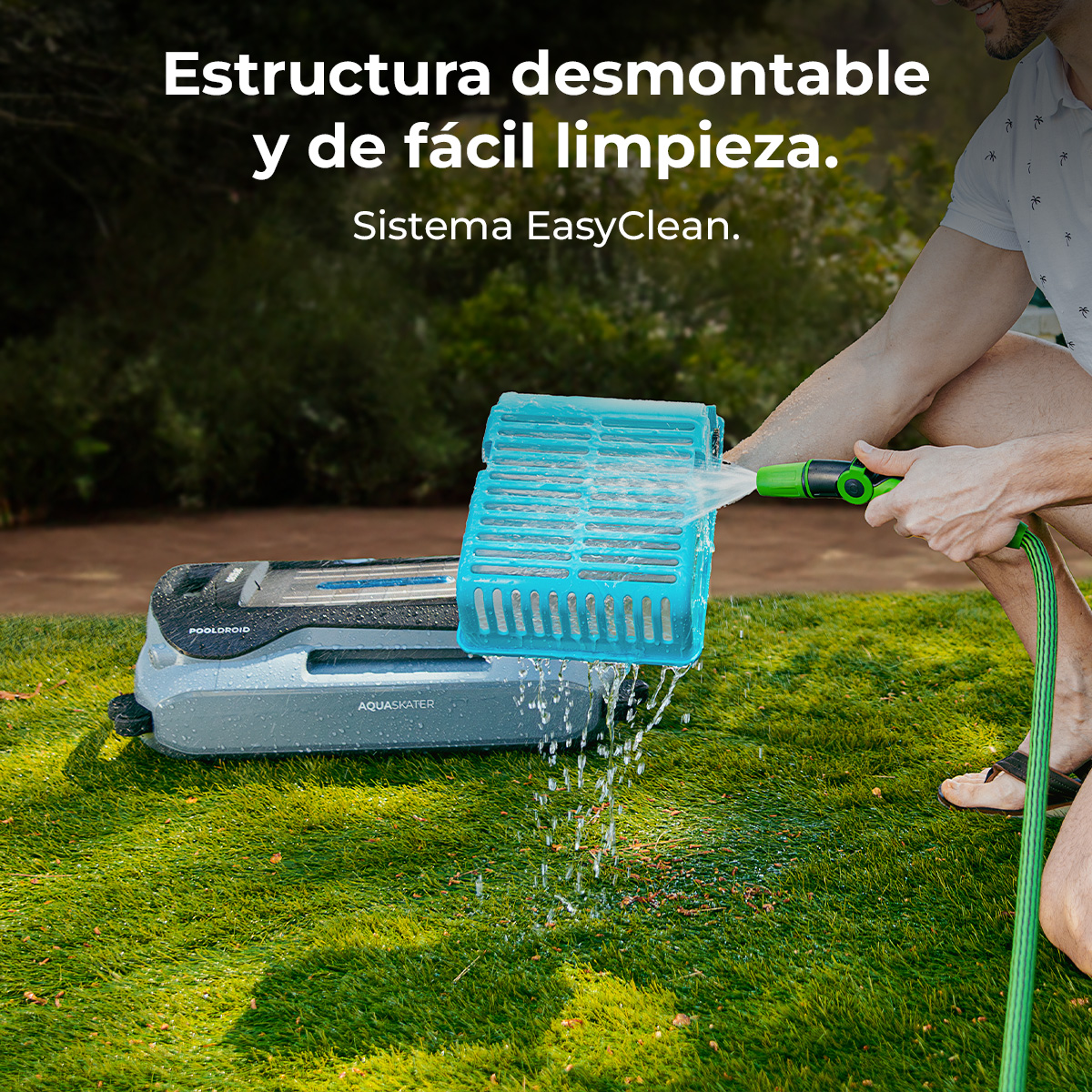 Un hombre limpia un filtro azul con una manguera de jardín sobre césped junto a un limpiafondos.
