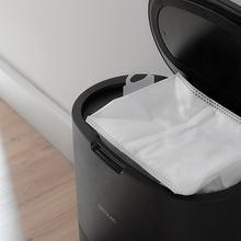Un cubo de basura negro con la tapa abierta, mostrando una bolsa blanca dentro.