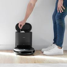 Un hombre con jeans azules y zapatillas blancas vacía un robot aspirador.