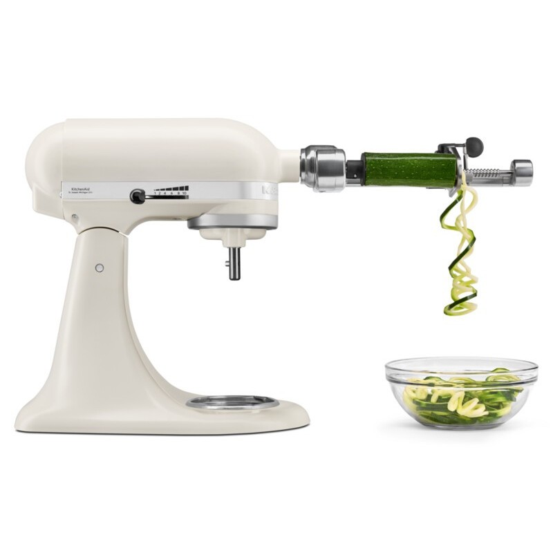 Un accesorio de batidora de pie KitchenAid color crema espiraliza un calabacín en un bol de fideos de calabacín.
