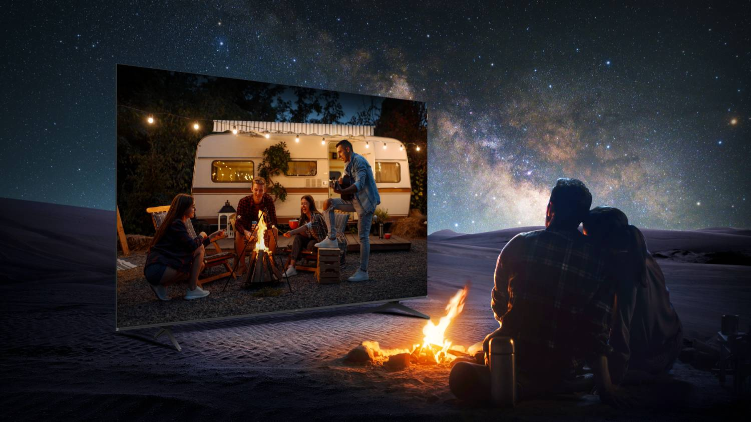 Pareja mira una caravana y fogata bajo un cielo estrellado.